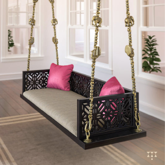 A wooden swing with cutwork, tinted in slate black with a decorative brass chain and animal motifs, fabric seat and cushions