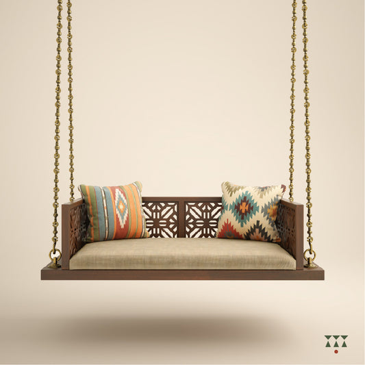 A handcrafted wooden swing with cutwork, tinted in tamarind brown with a decorative brass chain, fabric seat and cushions