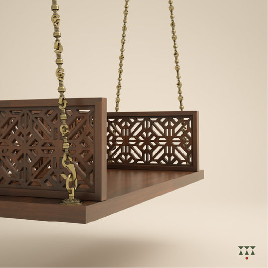 A handcrafted wooden swing with cutwork, tinted in tamarind brown with a decorative brass chain