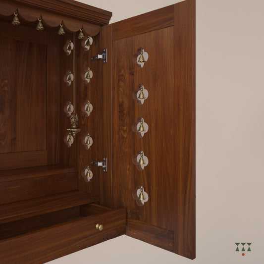A solid wood mandir with doors, pure brass bells, accessories, cutwork designs and storage tinted in almond brown