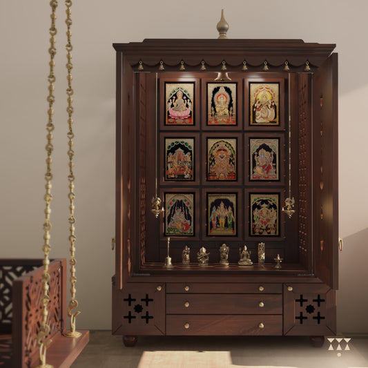 A solid wood mandir with pure brass bells, Tanjore art prints, cutwork designs and storage, tinted in a tamarind brown color