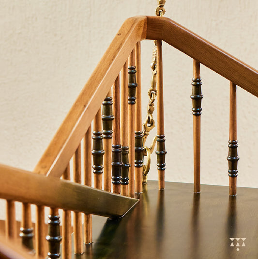Close up of a swing backrest with multiple sleek turned spindles tinted in brown and green and decorative brass chains