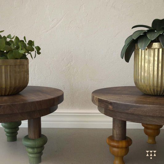 Close up of plants displayed on a set of low, solid wood accent tables in mocha brown with turned legs and contrasting tints