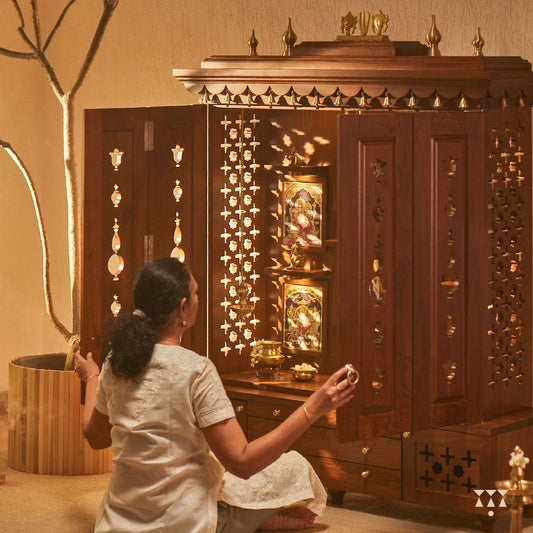 A solid wood mandir with doors, pure brass bells, accessories, cutwork designs and storage, tinted in an almond brown color