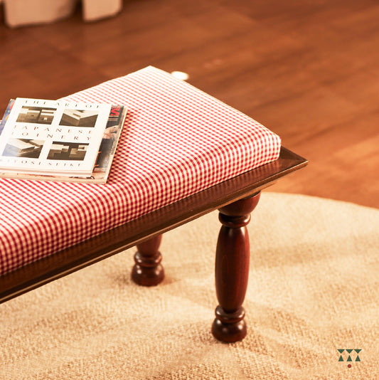 A handcrafted wooden bench with turned legs and a cushioned seat, upholstered in a luxurious checked silk