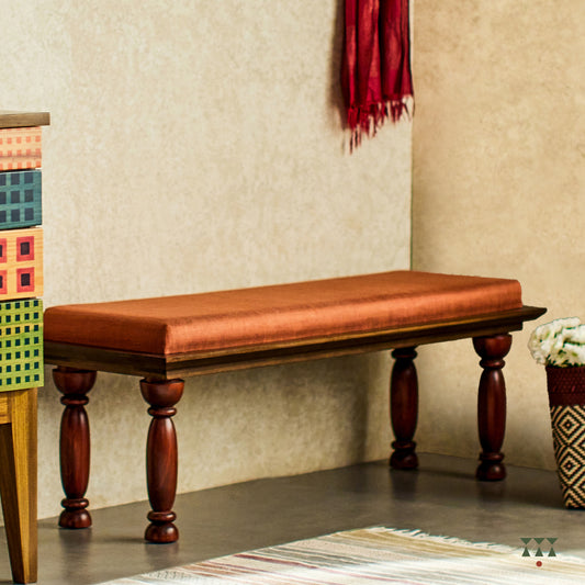 A solid wood bench with turned legs in a saffron orange tint and a cushioned seat upholstered in luxurious silk fabric