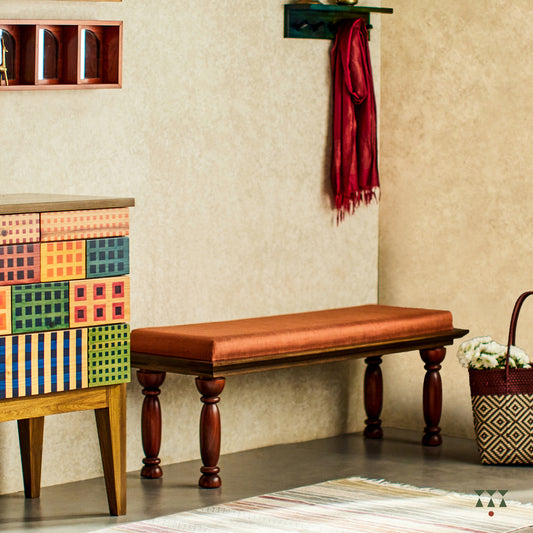 A solid wood bench with turned legs in a saffron orange tint and a cushioned seat upholstered in luxurious silk fabric