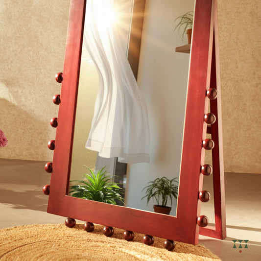 A closeup of the textural details at the bottom of a full-length solid wood mirror tinted in red