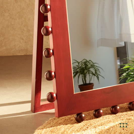 A closeup of the textural details at the bottom of a full-length solid wood mirror tinted in red