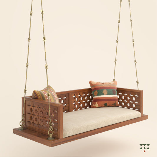 A wooden swing with cutwork patterns, tinted in almond brown with a decorative brass chain, and a fabric seat with cushions