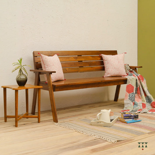 Wooden bench with pink cushions and a blanket in a room with a side table and decor items.