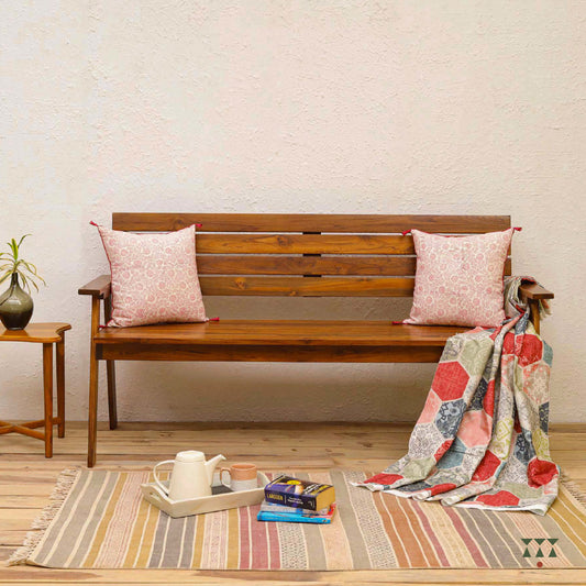 Wooden bench with cushions and a blanket on a striped rug in a room.