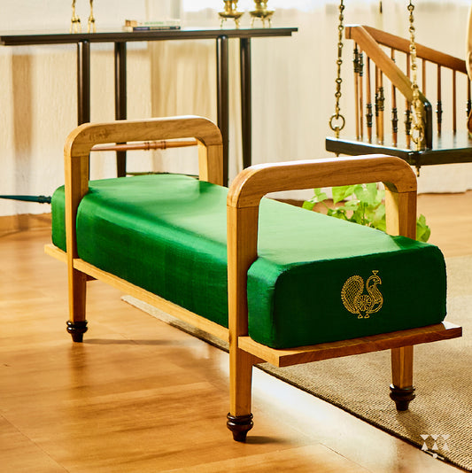 A sculptural solid wood long seat draped in green silk, with gold embroidered peacock motifs on the side