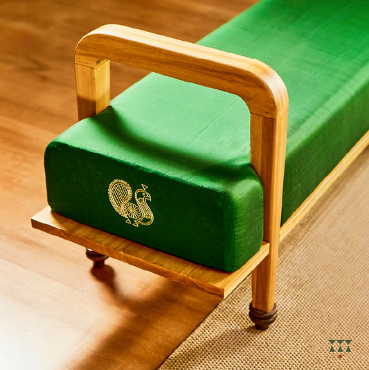 A sculptural solid wood long seat draped in green silk, with gold embroidered peacock motifs on the side