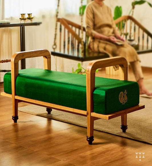 A sculptural solid wood long seat draped in green silk, with gold embroidered peacock motifs on the side