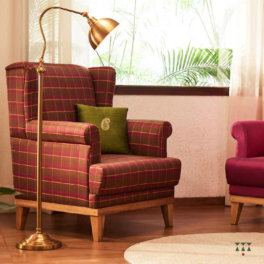 A solid wood wing chair draped in luxurious magenta and green checked silk, and a cushion embroidered with a paisley motif