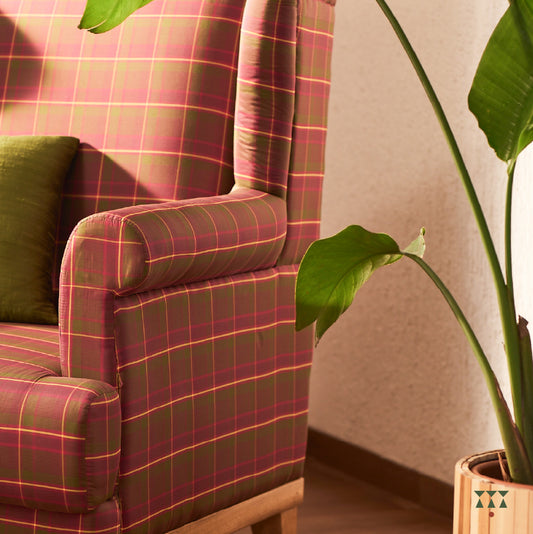 Close up of a wing chair draped in luxurious magenta and green checked silk crafted in solid wood