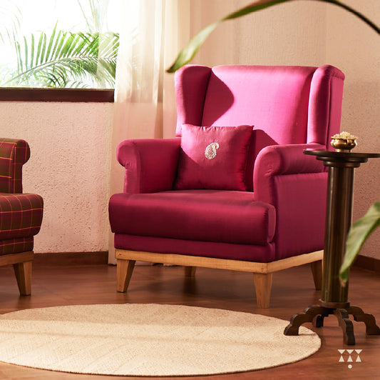 A solid wood wing chair draped in luxurious magenta silk and an embroidered cushion with a paisley motif