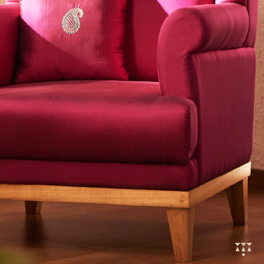 A solid wood wing chair draped in luxurious magenta silk and an embroidered cushion with a paisley motif