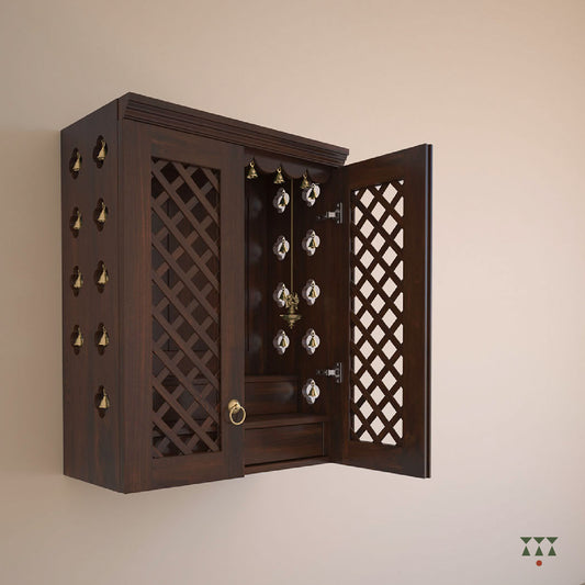 A solid wood, wall mounted Mandir with doors, pure brass accessories and storage to house idols. Tinted in tamarind brown
