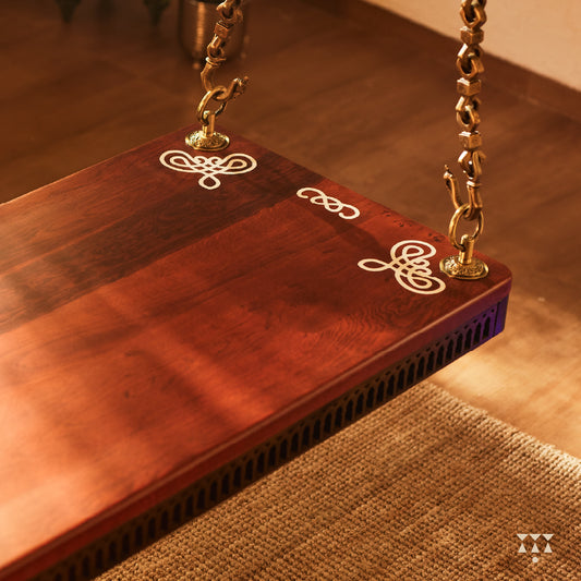 Close up of a solid wood swing with a pure brass animal motif chain and Kolam patterns inlayed in the seat
