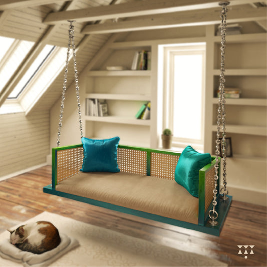 A wooden swing with weaving, tinted in Aqua Blue & Leaf Green with a decorative brass chain, and a fabric seat with cushions