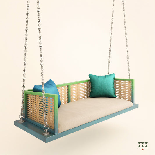 A wooden swing with weaving, tinted in Aqua Blue & Leaf Green with a decorative brass chain, and a fabric seat with cushions