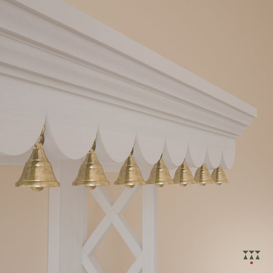 Close up of the scalloped edge and pure brass bells of a solid wood wall mounted Mandir, tinted in snow white
