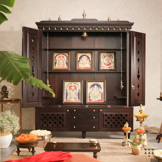 A solid wood mandir with pure brass bells, framed art prints, cutwork designs and storage, tinted in a tamarind brown color
