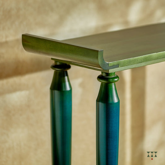 Close up of the curved edges and turned legs of a sculptural solid wood console table, tinted in Lagoon Blue & Moringa Green