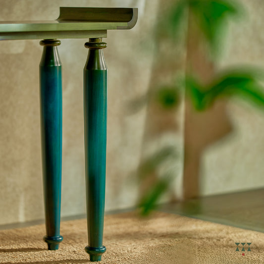 Close up of the curved edges and turned legs of a sculptural solid wood console table, tinted in Lagoon Blue & Moringa Green