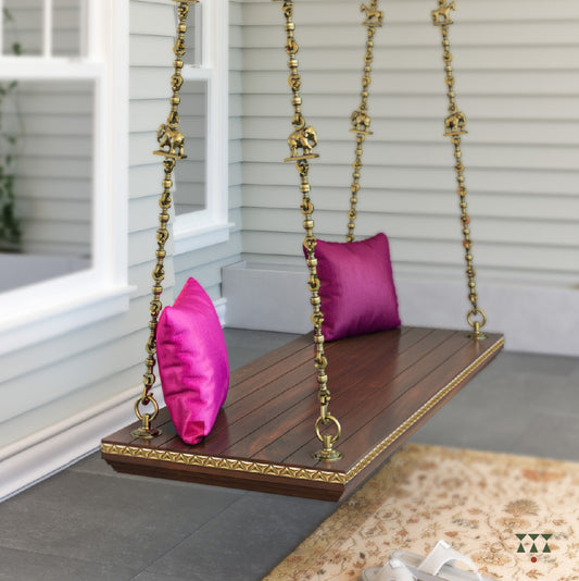 A solid wood swing base tinted in tamarind brown with decorative edging and brass chains with animal motifs and cushions