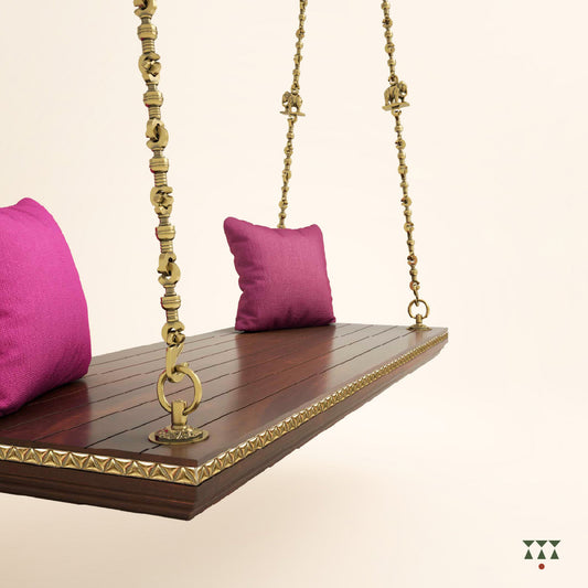 A solid wood swing base tinted in tamarind brown with decorative edging and brass chains with animal motifs and cushions