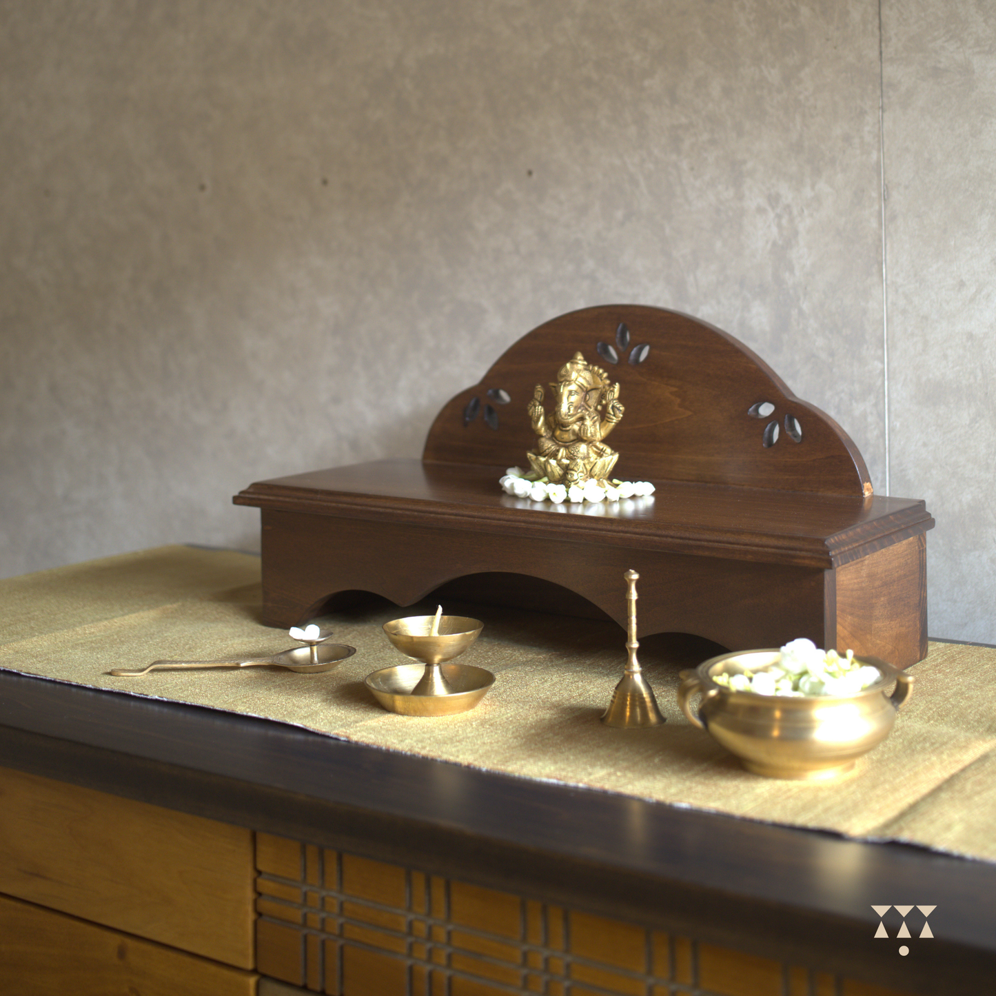Wooden pooja platform placed on a table with religious brass decor.