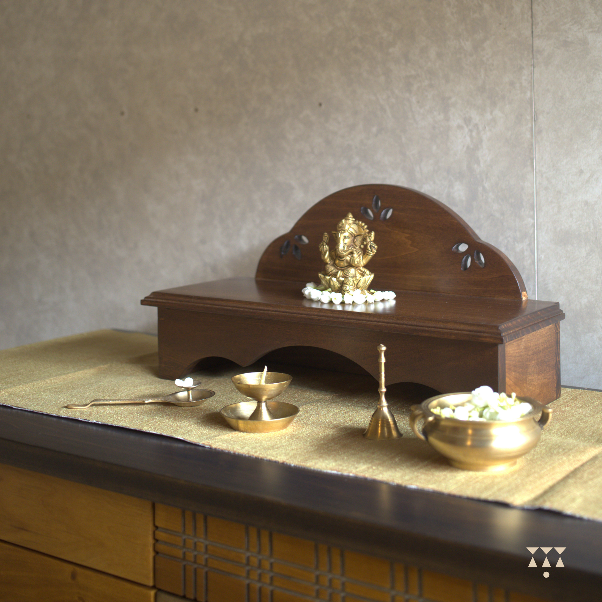Wooden pooja platform placed on a table with religious brass decor.