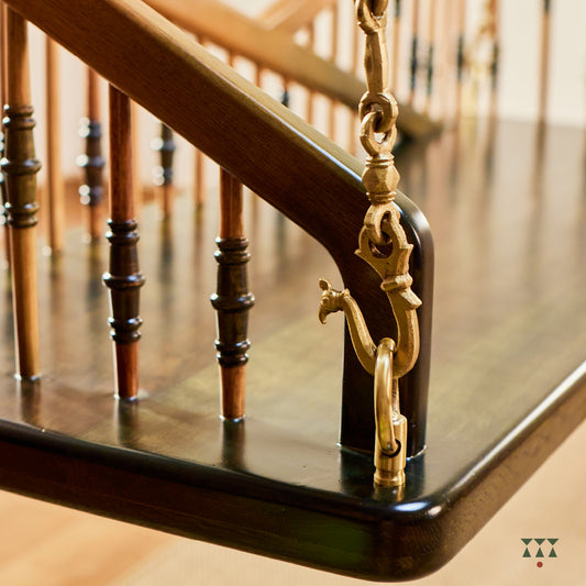 Close up of a swing backrest with multiple sleek turned spindles tinted in brown and green and decorative brass chains