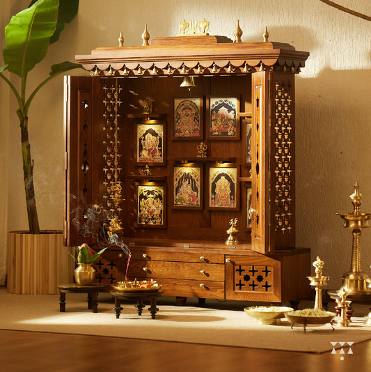 A solid wood mandir with pure brass bells, Tanjore art prints, cutwork designs and storage, tinted in an almond brown color
