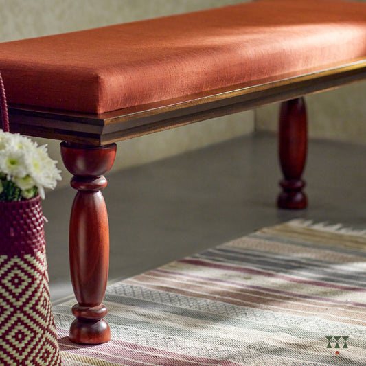 A solid wood bench with turned legs in a saffron orange tint and a cushioned seat upholstered in luxurious silk fabric 