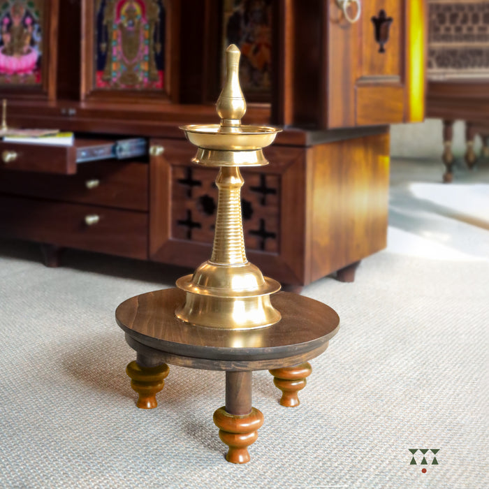 Brass Lamp on a wooden table on a textured surface with wooden home temple in the background
