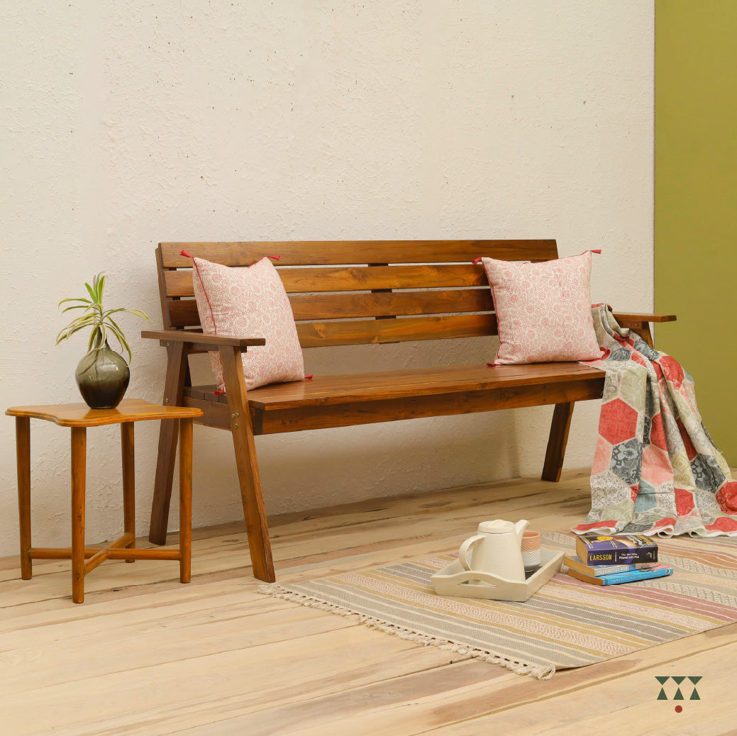 Wooden bench with pink cushions and a blanket in a room with a side table and decor items.