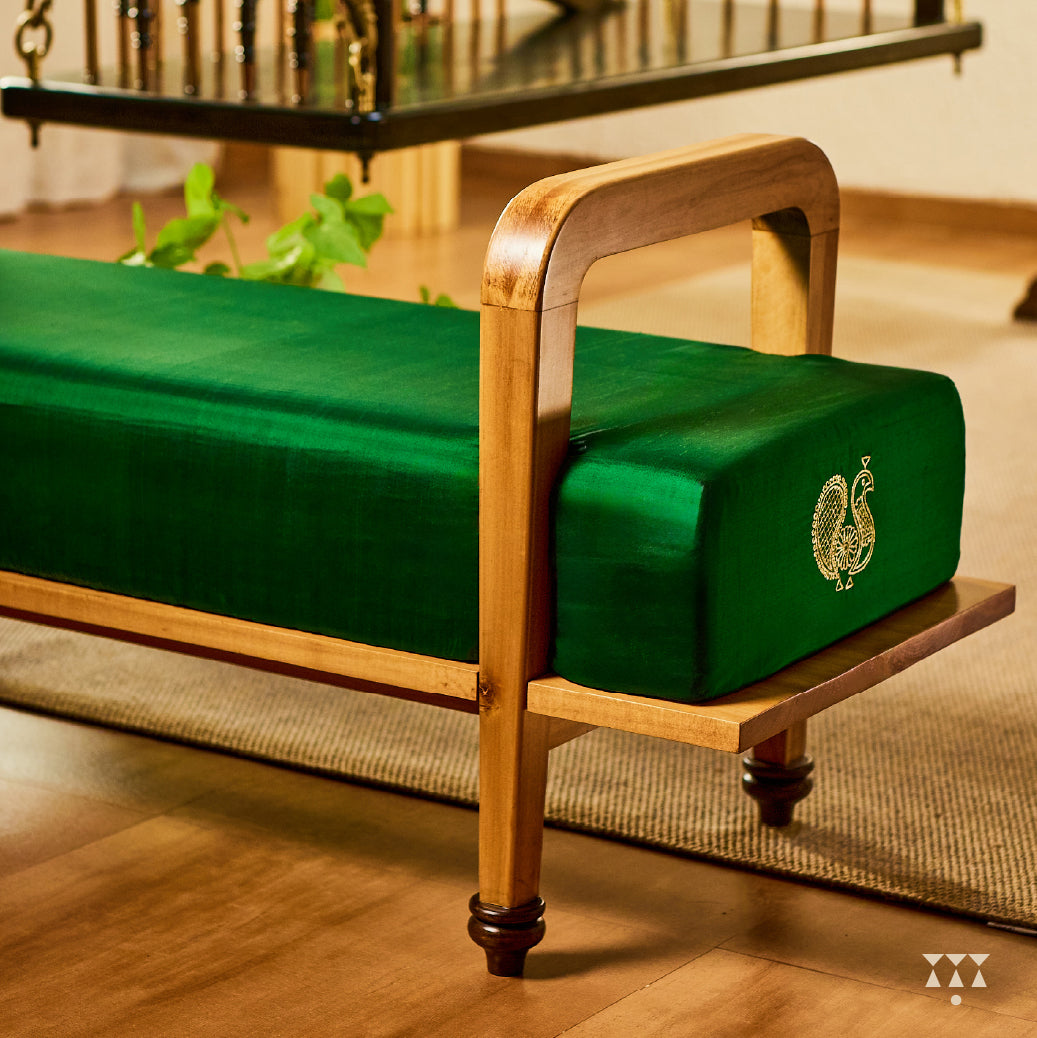 A sculptural solid wood long seat draped in green silk, with gold embroidered peacock motifs on the side