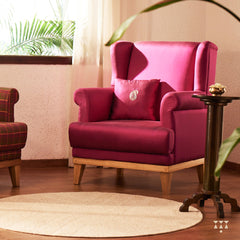 A solid wood wing chair draped in luxurious magenta silk and an embroidered cushion with a paisley motif