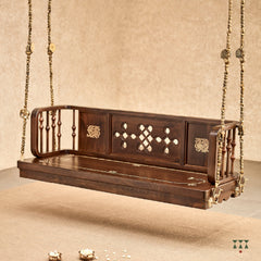 A close up of a wooden swing crafted with Kolam, Annapakshi and floral designs and turning details on the backrest and seat 