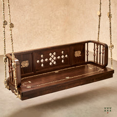 A close up of a wooden swing crafted with Kolam, Annapakshi and floral designs and turning details on the backrest and seat 