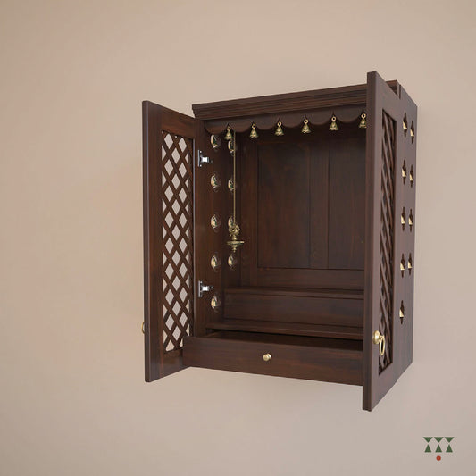 A solid wood, wall mounted Mandir with doors, brass accessories and storage to house idols. Tinted in tamarind brown.