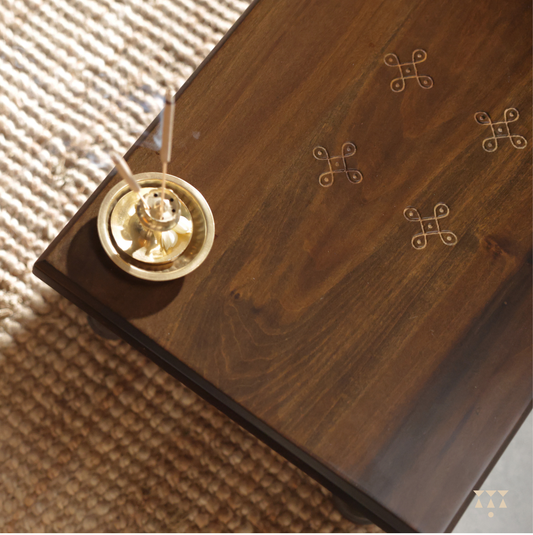 kolam patterns on a wooden table with incense burner placed on it.