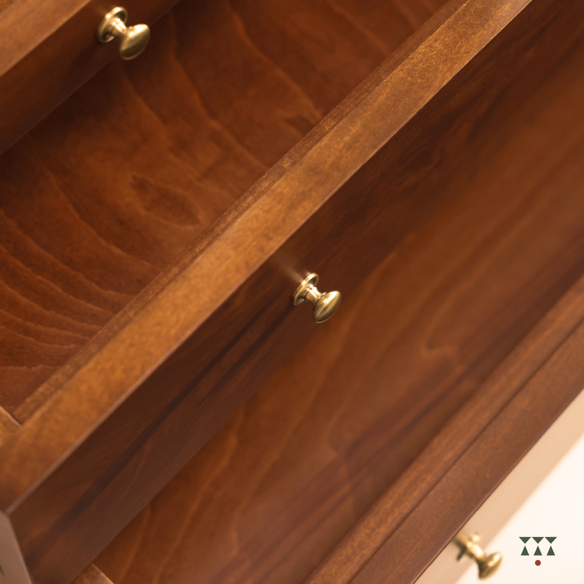 Close-up of a wooden drawer front with warm medium-brown wood grain and small round brass knobs.