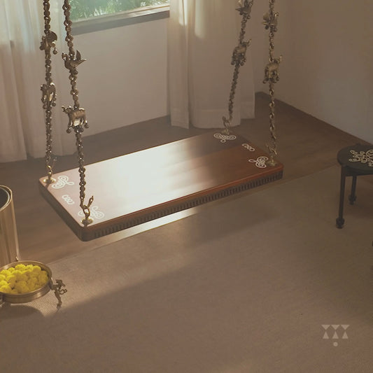 Video of a solid wood swing in gentle motion with a pure brass animal motif chain and Kolam patterns inlayed in the seat